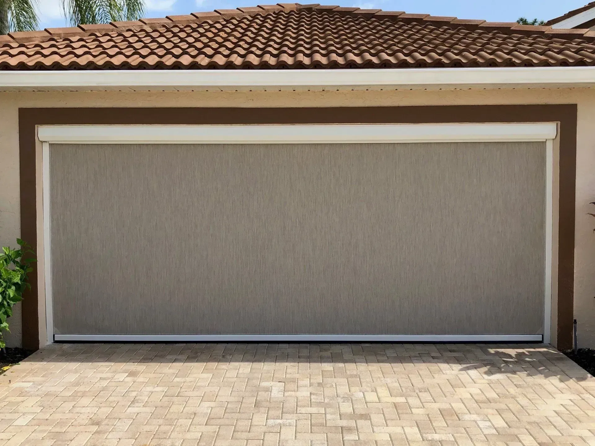 Tan garage door screen on a light brown building with a brick driveway.