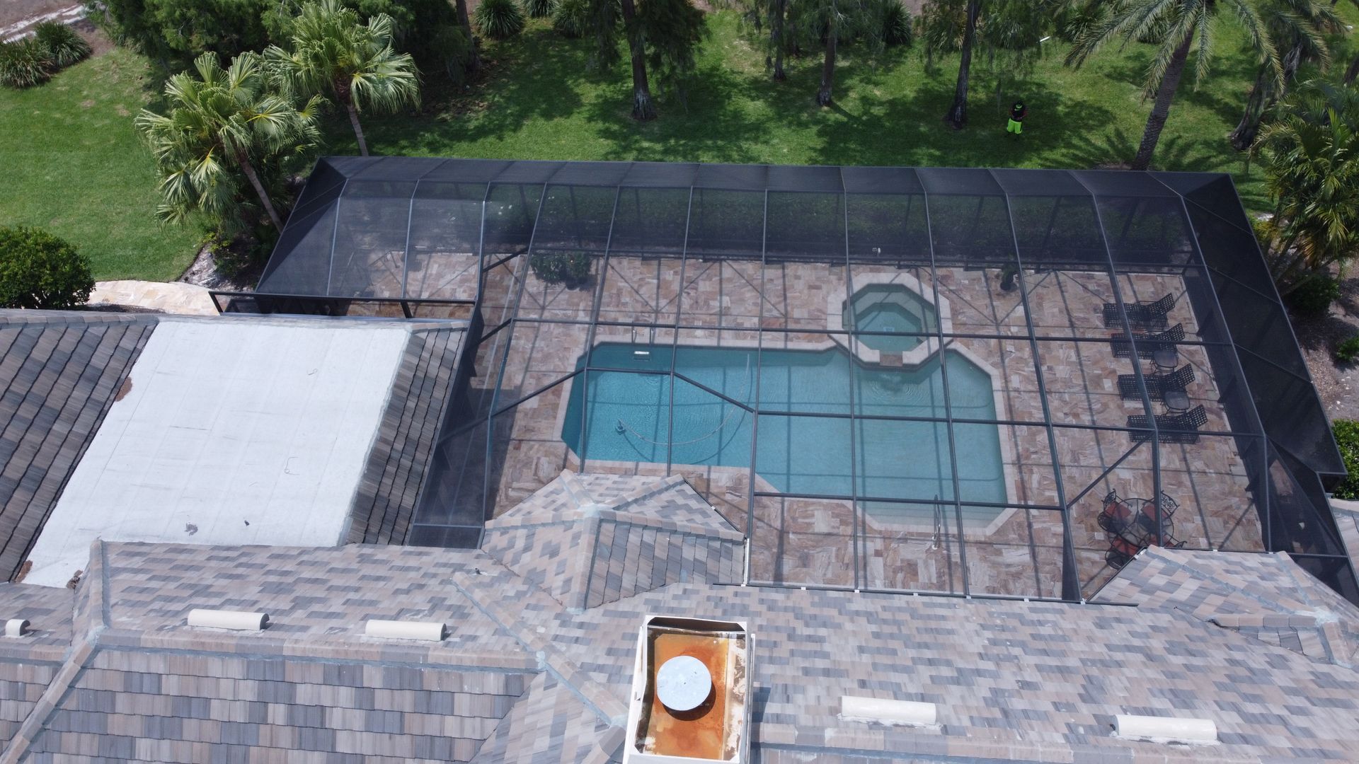 Overhead view of a house with a screened-in pool and hot tub surrounded by tile.