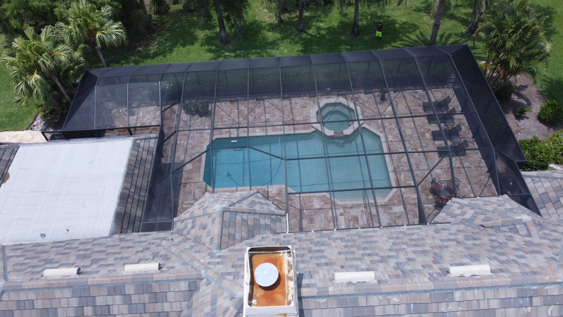Aerial view of a swimming pool enclosed by a screen structure, on a house's rooftop.