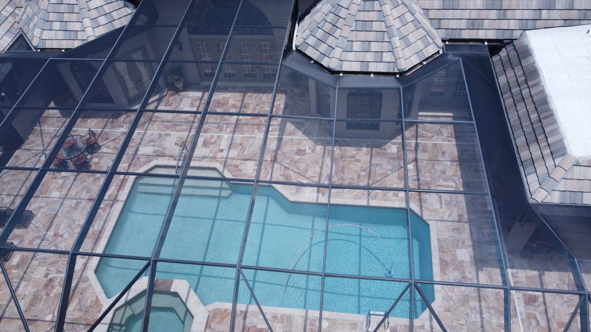 Overhead view of a pool inside a screened patio, adjacent to a home with a tiled roof.
