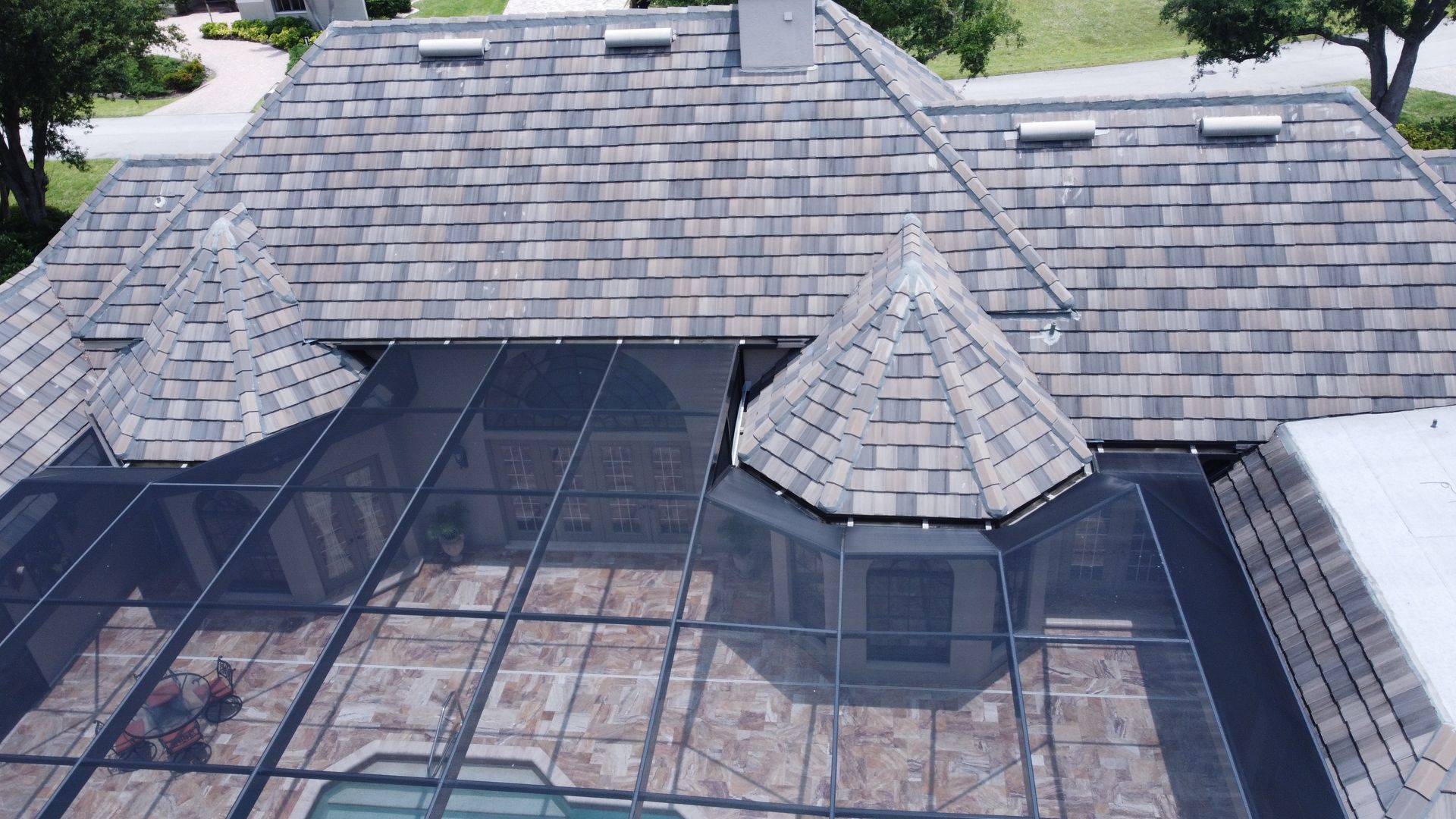 Aerial view of a home with a gray shingled roof, a glass-covered enclosure, and a landscaped yard.