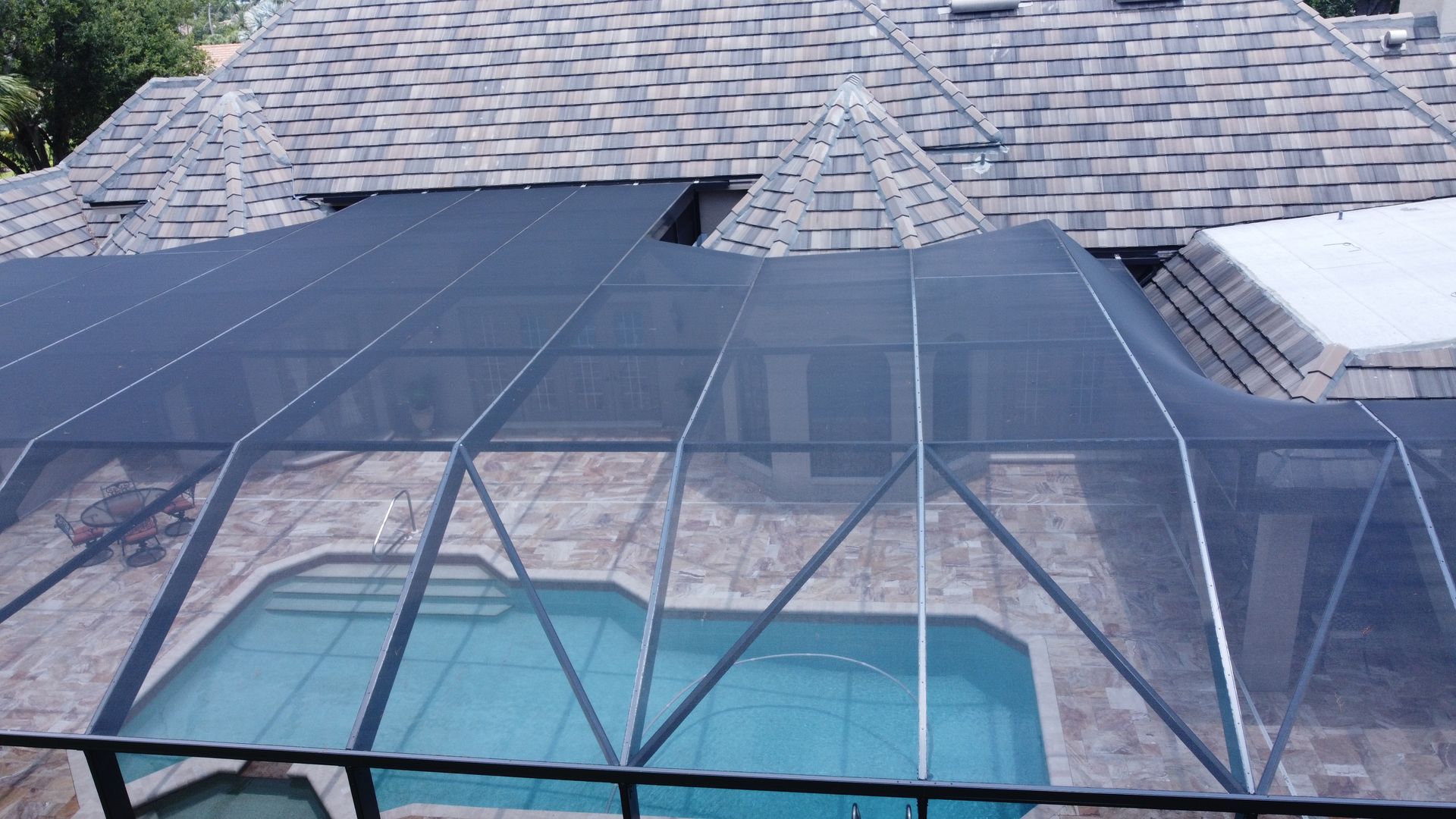 Pool enclosure with black mesh and metal frame, covering a blue pool. Roof visible above.
