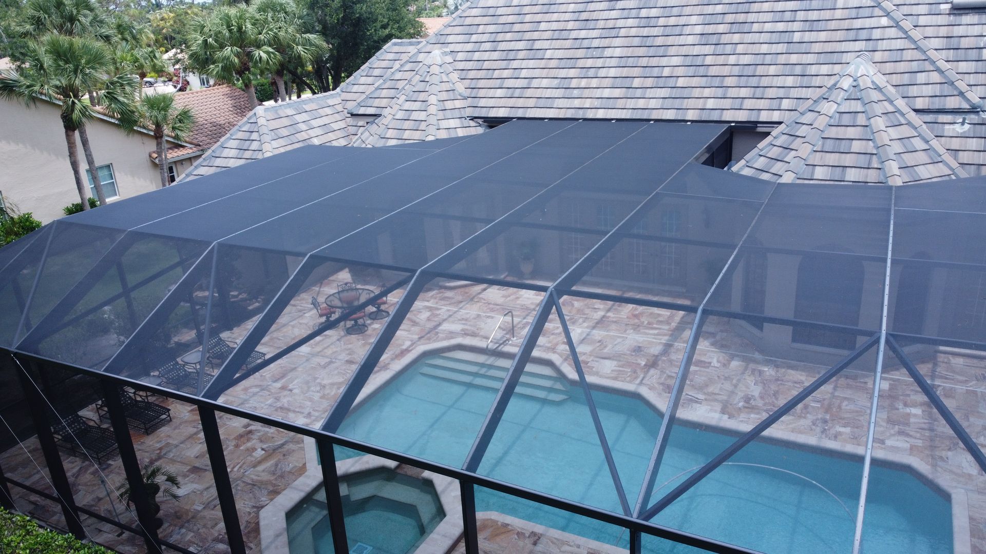 Pool enclosed by black mesh screen structure; tile roof and landscaping in background.