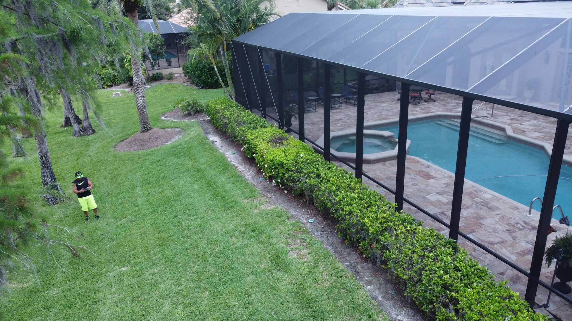 Man standing on green lawn beside a screened pool area with bushes.