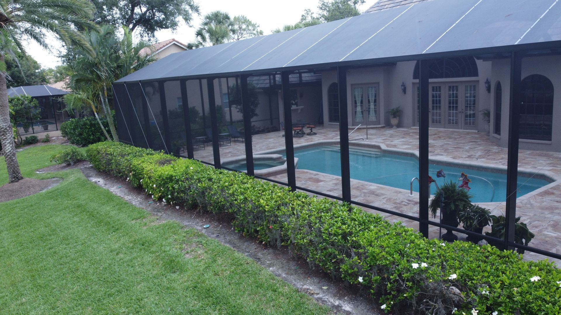A screened-in pool area with black fencing, surrounded by greenery and a house.