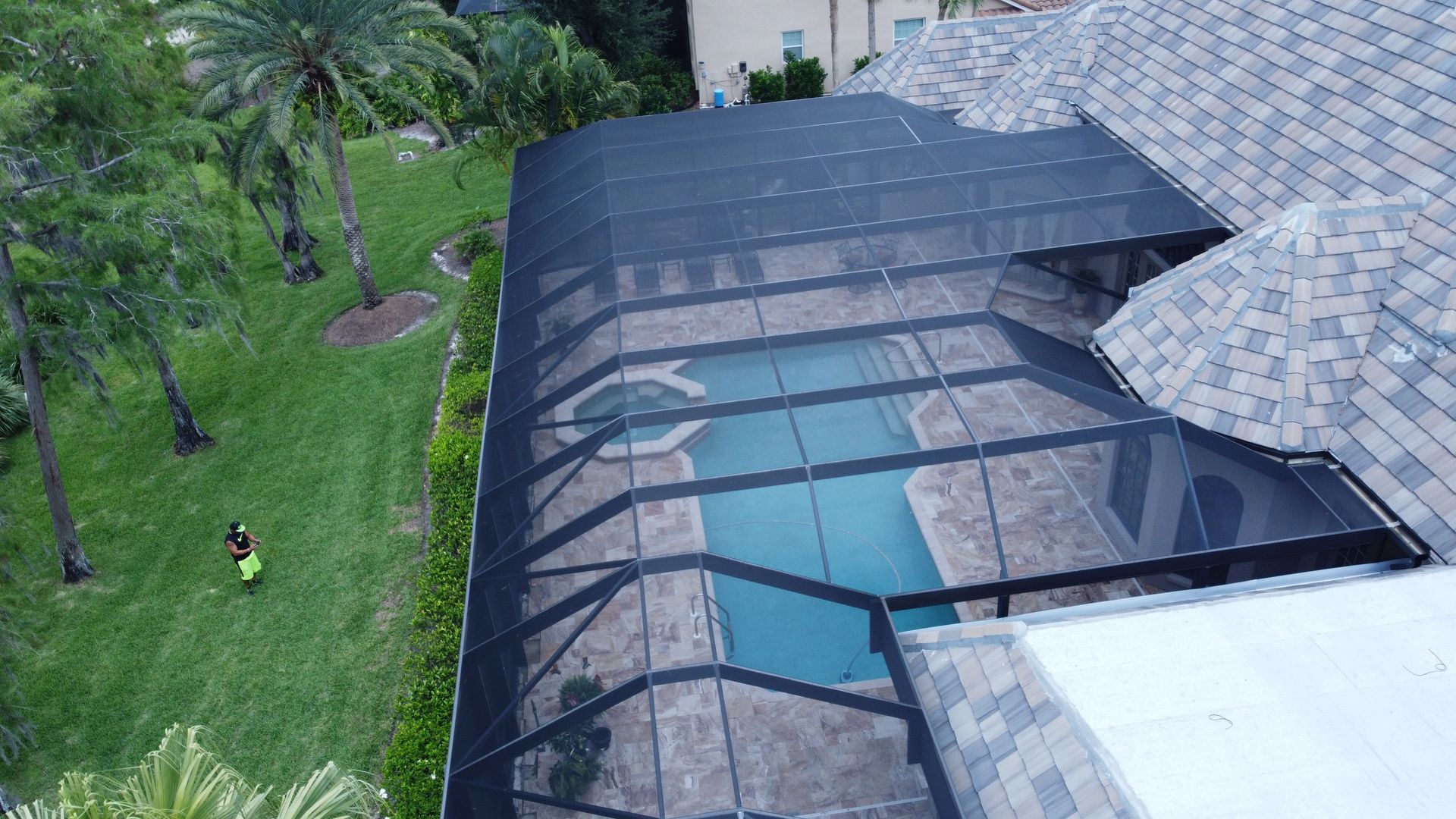 Pool enclosed by a black screen structure, adjacent to a house with a tiled roof and grassy yard.