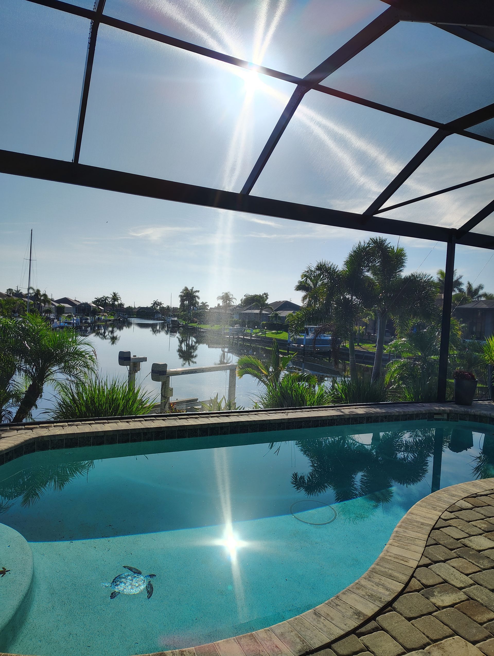 Pool with sunny water view, screened enclosure. Bright sun reflects on water.