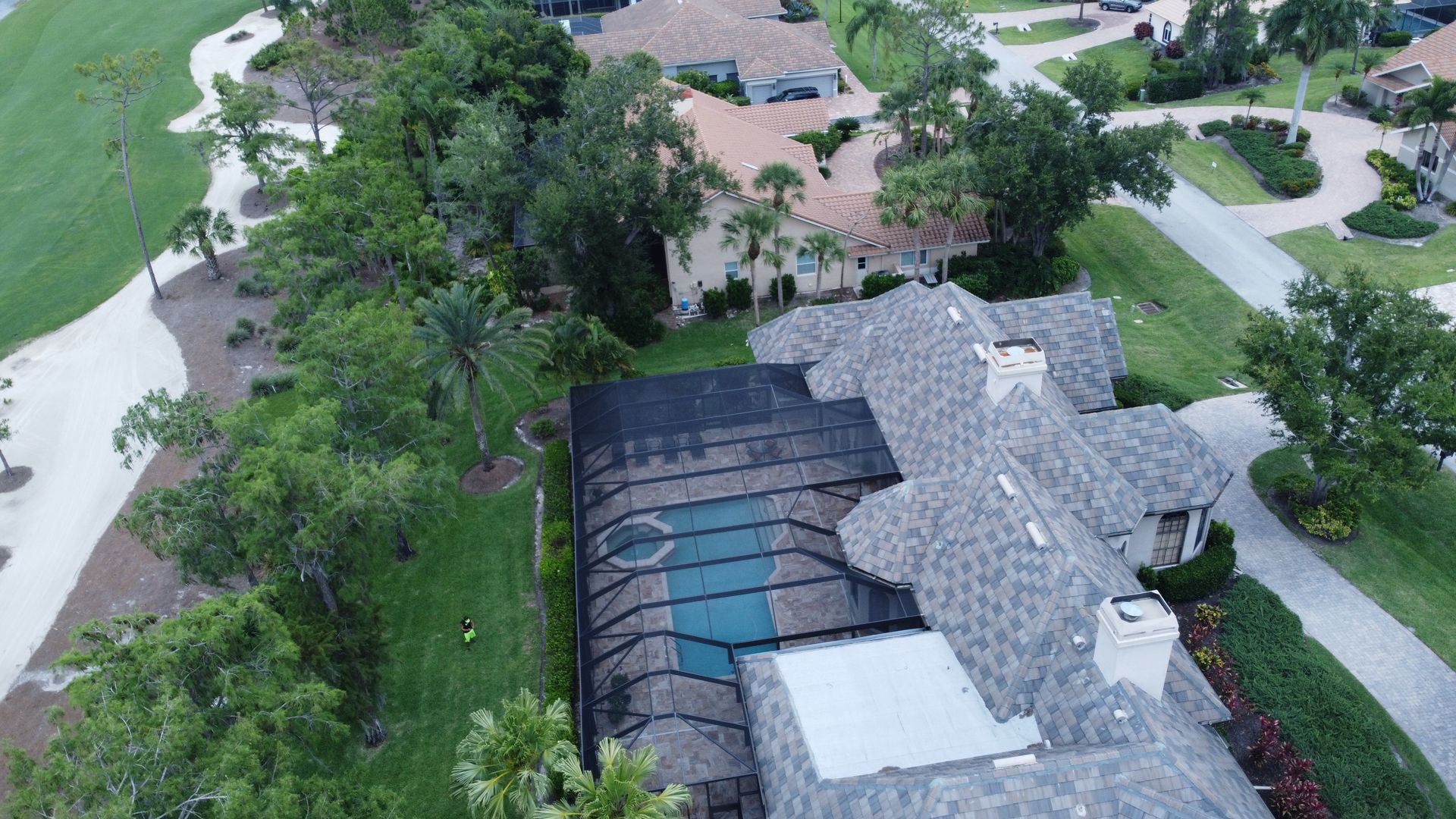 Aerial view of a house with a pool and golf course nearby, surrounded by lush green trees.