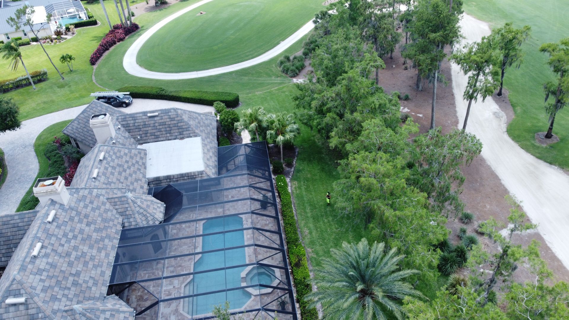 Aerial view of a house with a pool, golf course, and trees. A car is parked near the house.