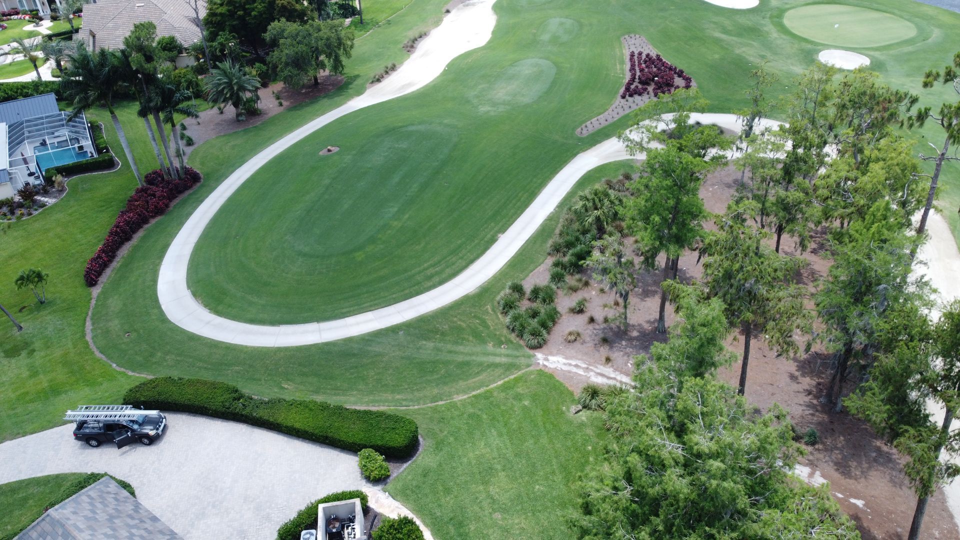 Aerial view of a green golf course with a winding path, sand traps, and trees.