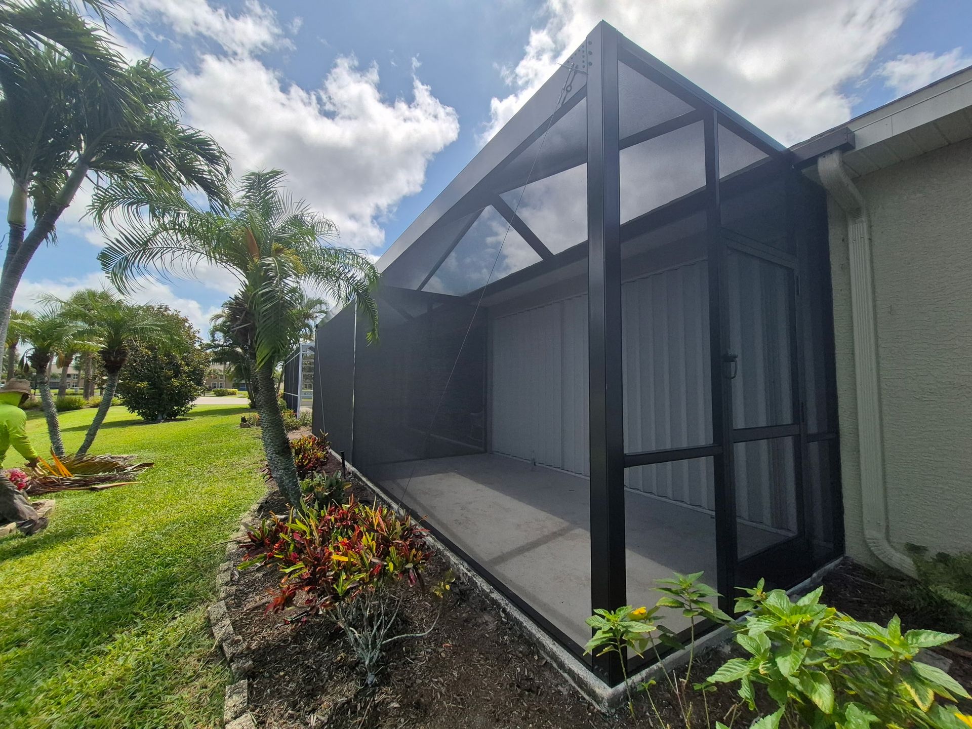 Screened-in patio with black frame, gray walls, and lush landscaping on a sunny day.