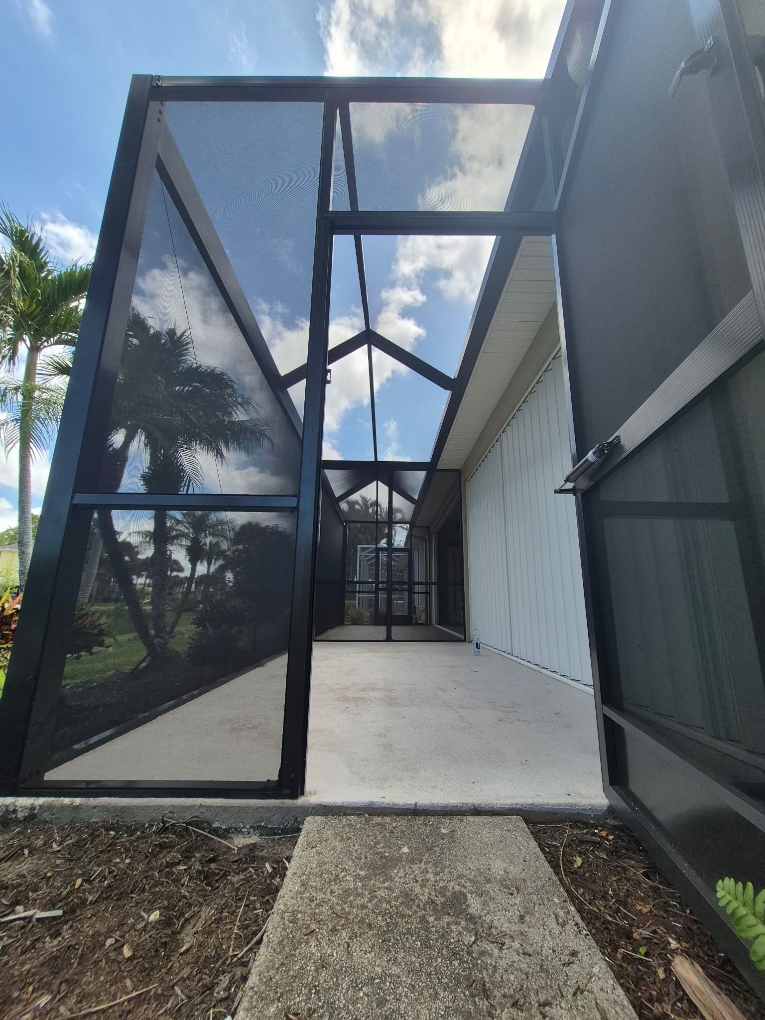 Black screened enclosure over a concrete patio with a view of a yard and sky.