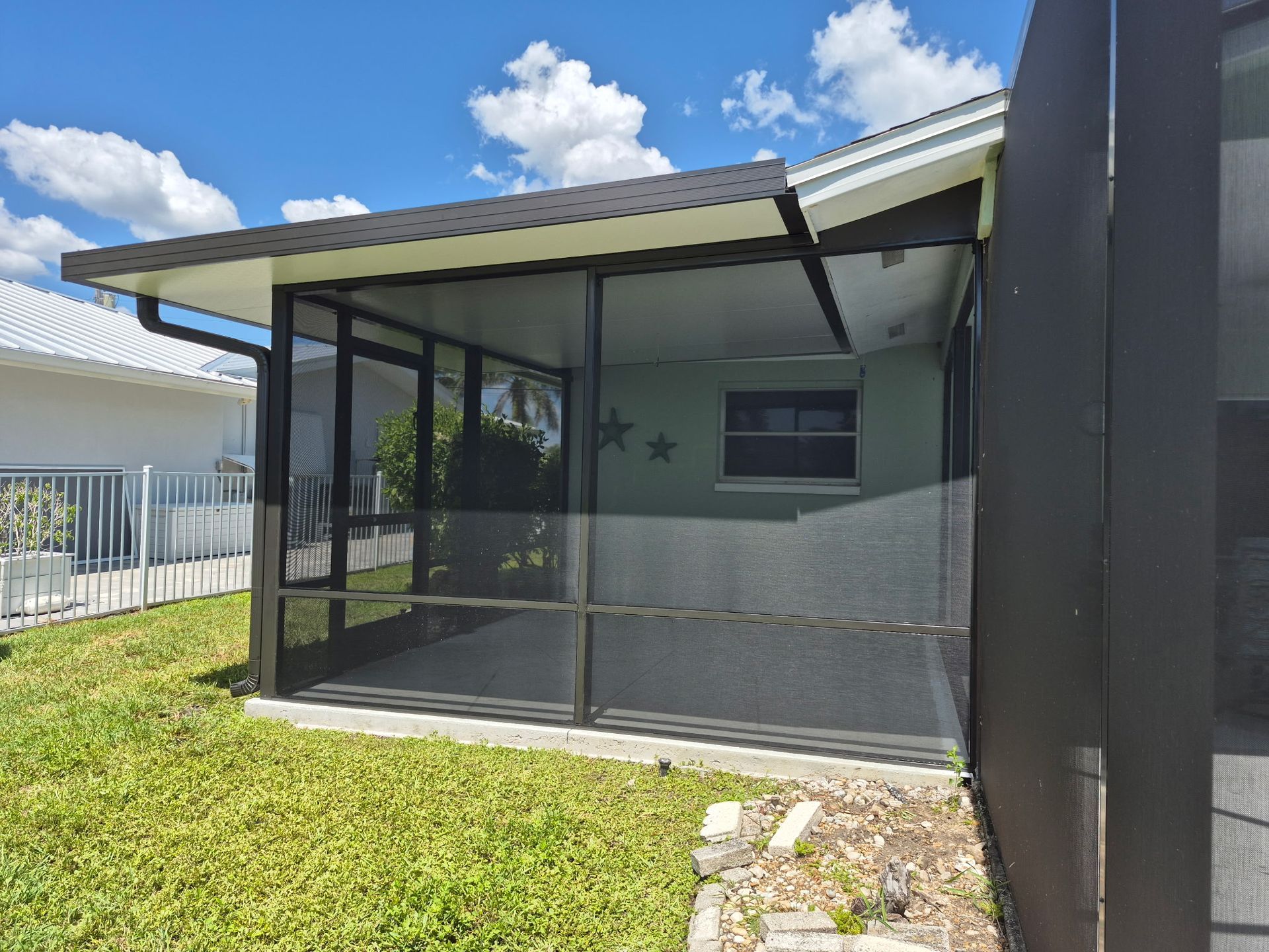 Screened patio with black frame, green grass, light blue walls, and a clear blue sky.