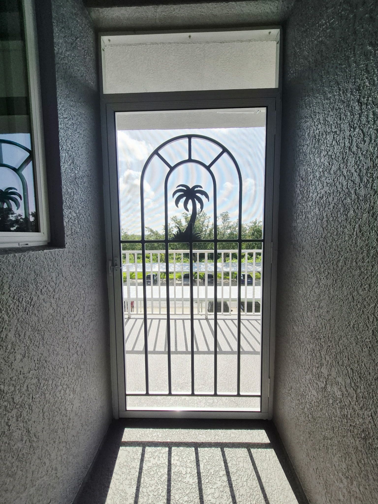 Metal security door with palm tree design, leading to an outdoor balcony.