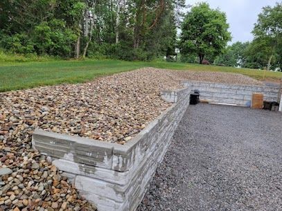 Stone retaining wall with gravel top beside a grassy yard and gravel driveway