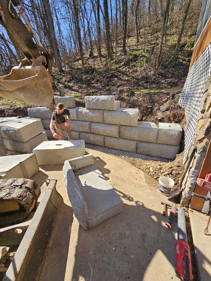 Person sitting in a dirt work area beside stacked concrete blocks and a retaining wall under construction