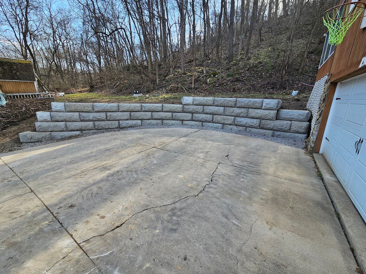 Concrete driveway with stone retaining wall and leafless trees in the background