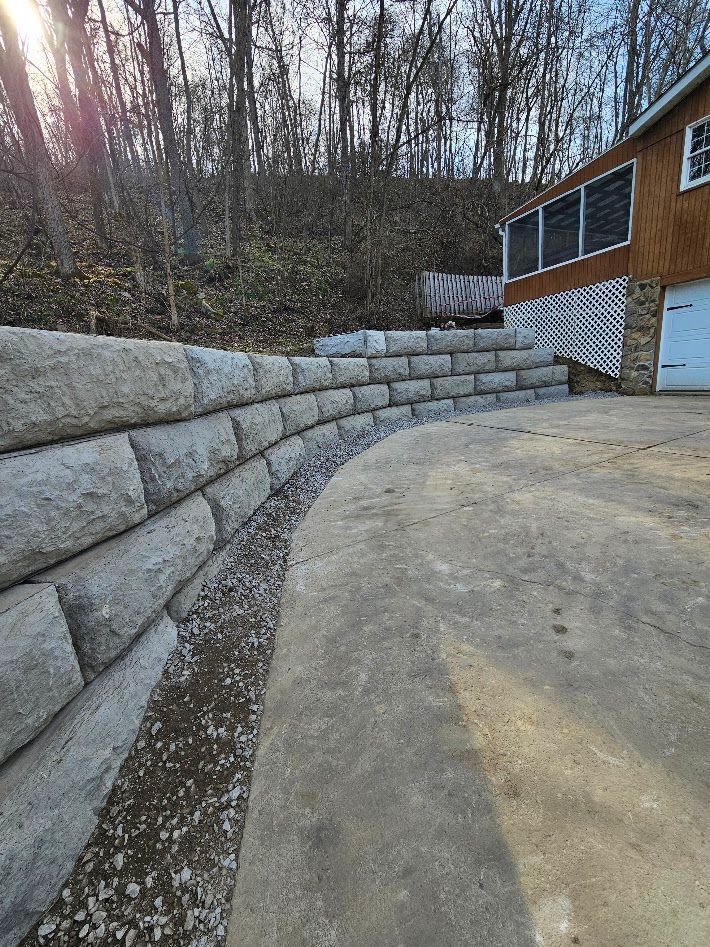 Curved stacked-stone retaining wall beside a concrete driveway and a house