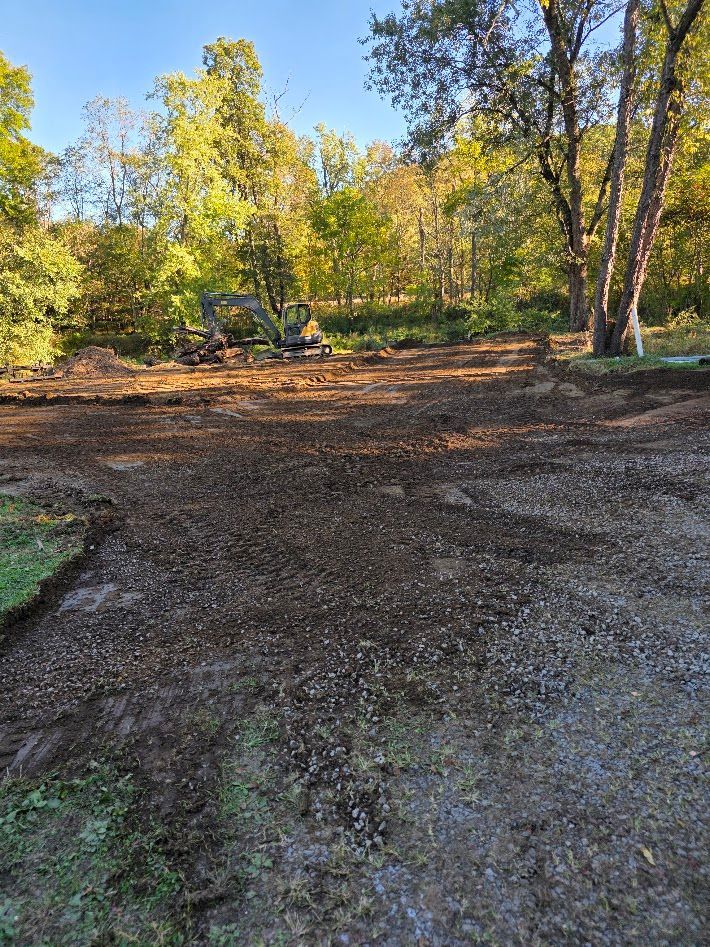 Gravel clearing in a wooded area with autumn trees and blue sky overhead