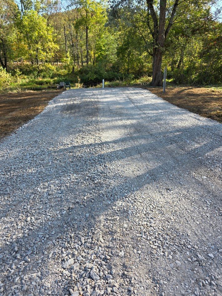 Freshly spread gravel driveway in a wooded area with trees and sunlight shadows