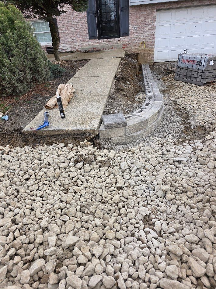 Front walkway under construction beside a house, with gravel, stone edging, and a drill on the path.