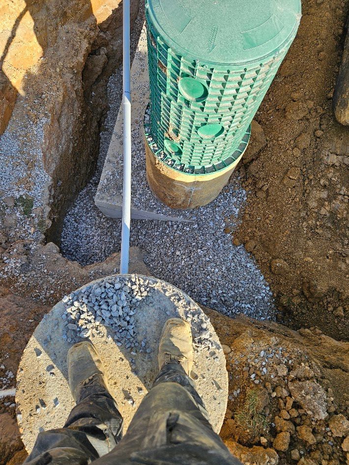 Boots on gravel beside a green utility pipe in a dirt trench