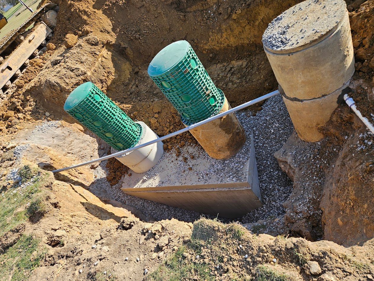 Utility pipes with green mesh covers and concrete caps exposed in a dirt excavation.