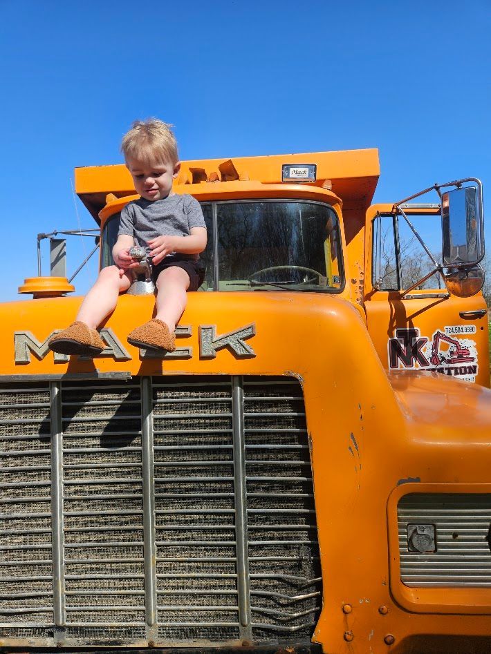 Child sitting on the hood of an orange truck under a blue sky