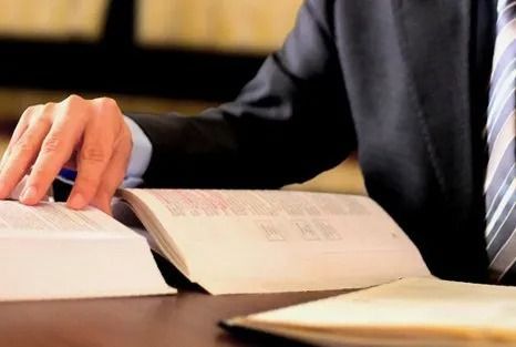Person in a suit reviewing open books on a desk, possibly studying legal documents.
