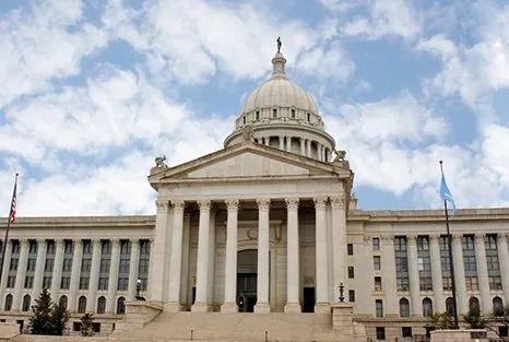 Oklahoma State Capitol building with white columns and dome, blue sky background.
