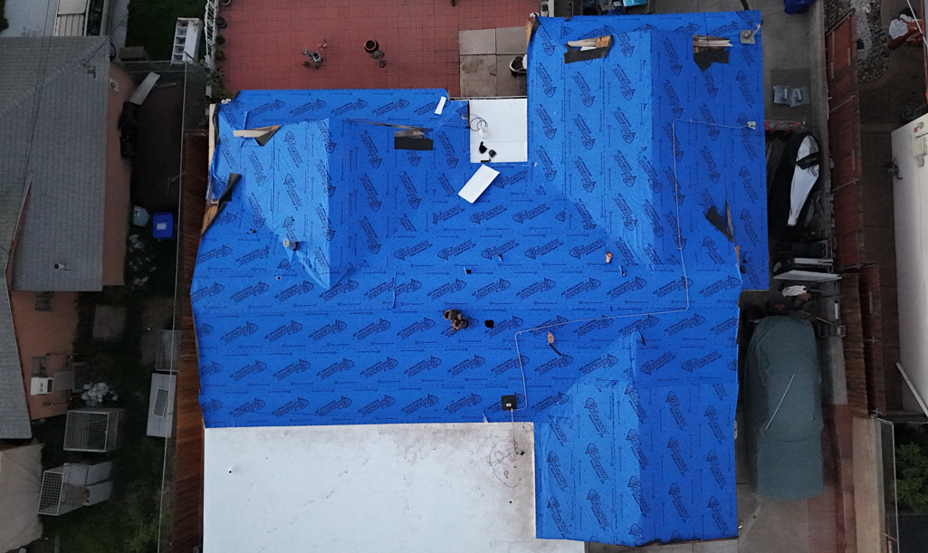 Blue tarp covering most of a rooftop between neighboring buildings, aerial view
