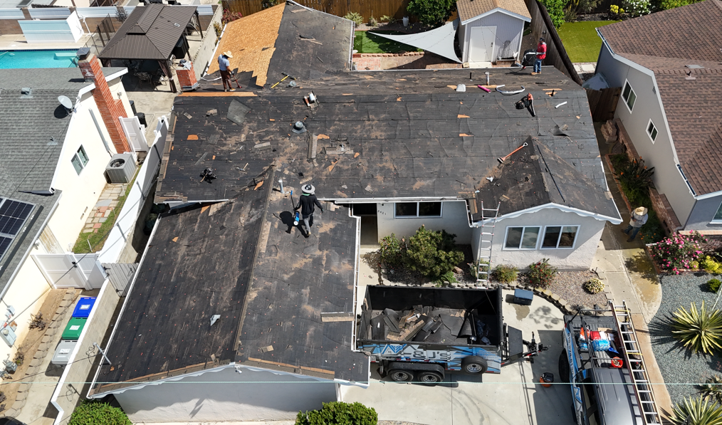 Aerial view of a house with a damaged dark roof and workers repairing it.