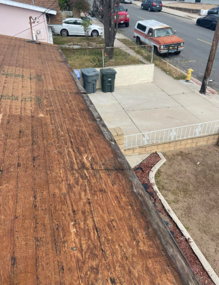 Rooftop view of a residential street with a wooden roof, driveway, trash bins, and parked cars.
