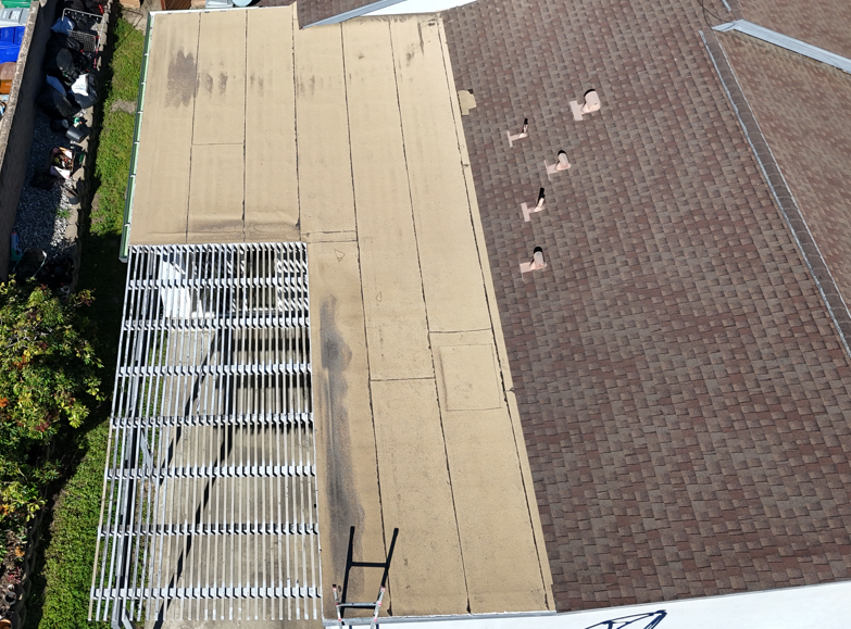 Aerial view of a tan rooftop with HVAC units beside a brown shingled roof.