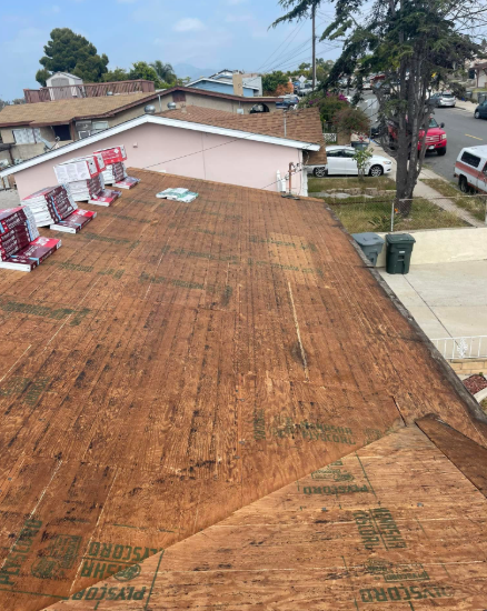 House roof under repair with new underlayment, ladders, and shingles stacked along the left edge