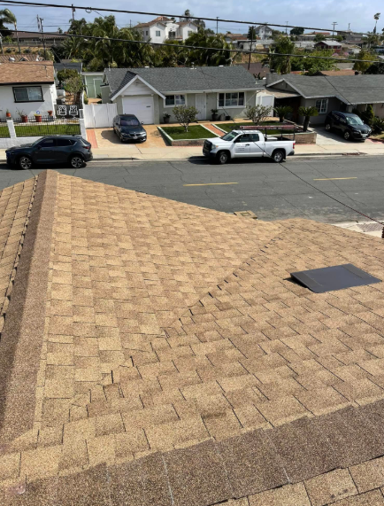 Tan shingled roof in foreground, with houses, parked cars, and a street across the road