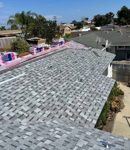 Roof under construction with gray shingles and stacks of pink materials along the ridge