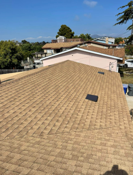 Tan shingle roof with two black vents, viewed from above on a sunny day.
