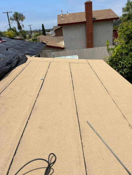 Roofing underlayment on a rooftop, with a chimney and neighboring houses in view.