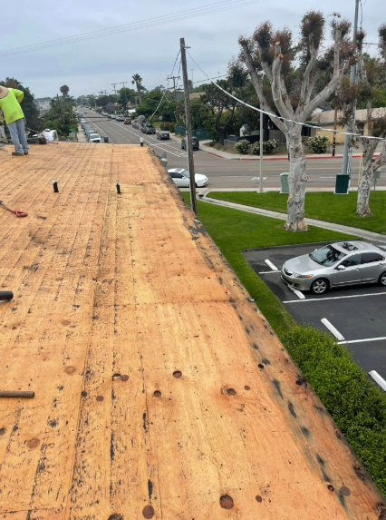 Workers installing roofing on a flat roof beside a parking lot and street after a storm