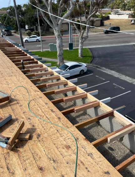 Roof under construction with exposed wooden framing beside a street and parked cars.