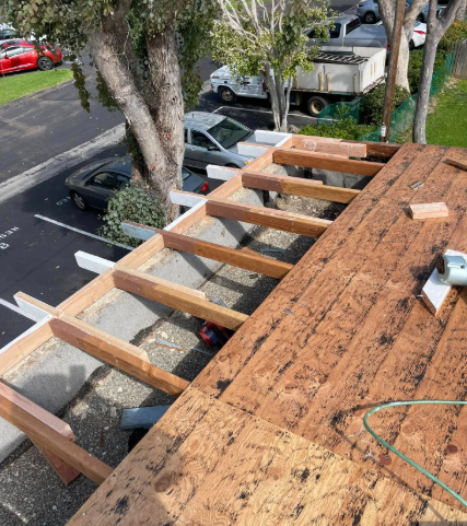 Roof under construction with exposed wooden framing beside a parking lot and parked cars