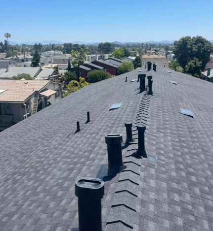 Rooftop with black vent pipes overlooking a suburban neighborhood and distant mountains under a clear blue sky