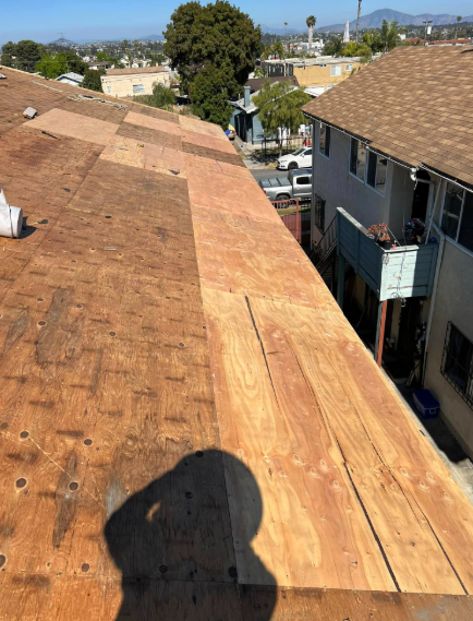 Rooftop with weathered shingles overlooking apartment buildings and a street on a clear day