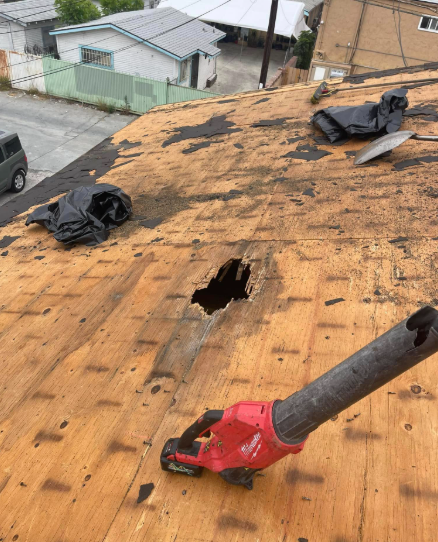 Damaged plywood roof with a large hole and a red tool on top, viewed from above