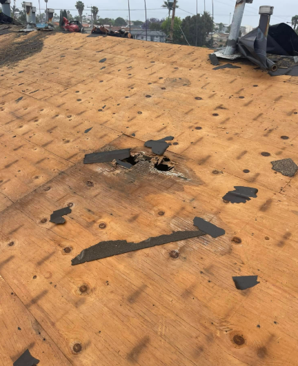 Damaged tan roof with torn shingles and a hole near the ridge, debris scattered around.