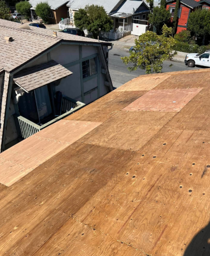 Wooden roof sheathing on a house under construction, viewed from the rooftop with neighboring homes below