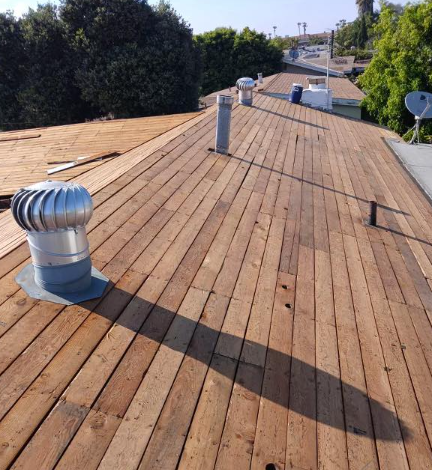 Rooftop with wooden decking and metal vents, viewed under bright sunlight.