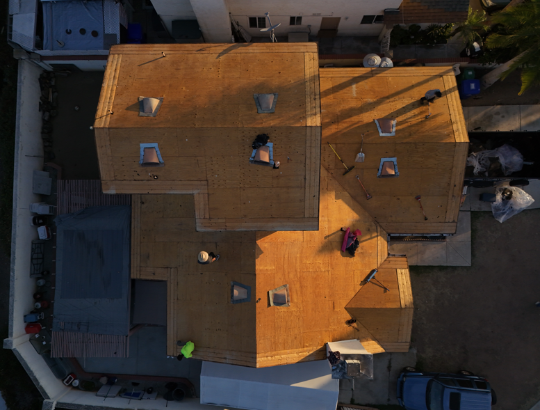 Aerial view of orange-roofed houses in a residential neighborhood, with shadows and parked cars.