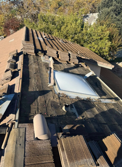 Damaged shingle roof with missing sections and a skylight, viewed from above